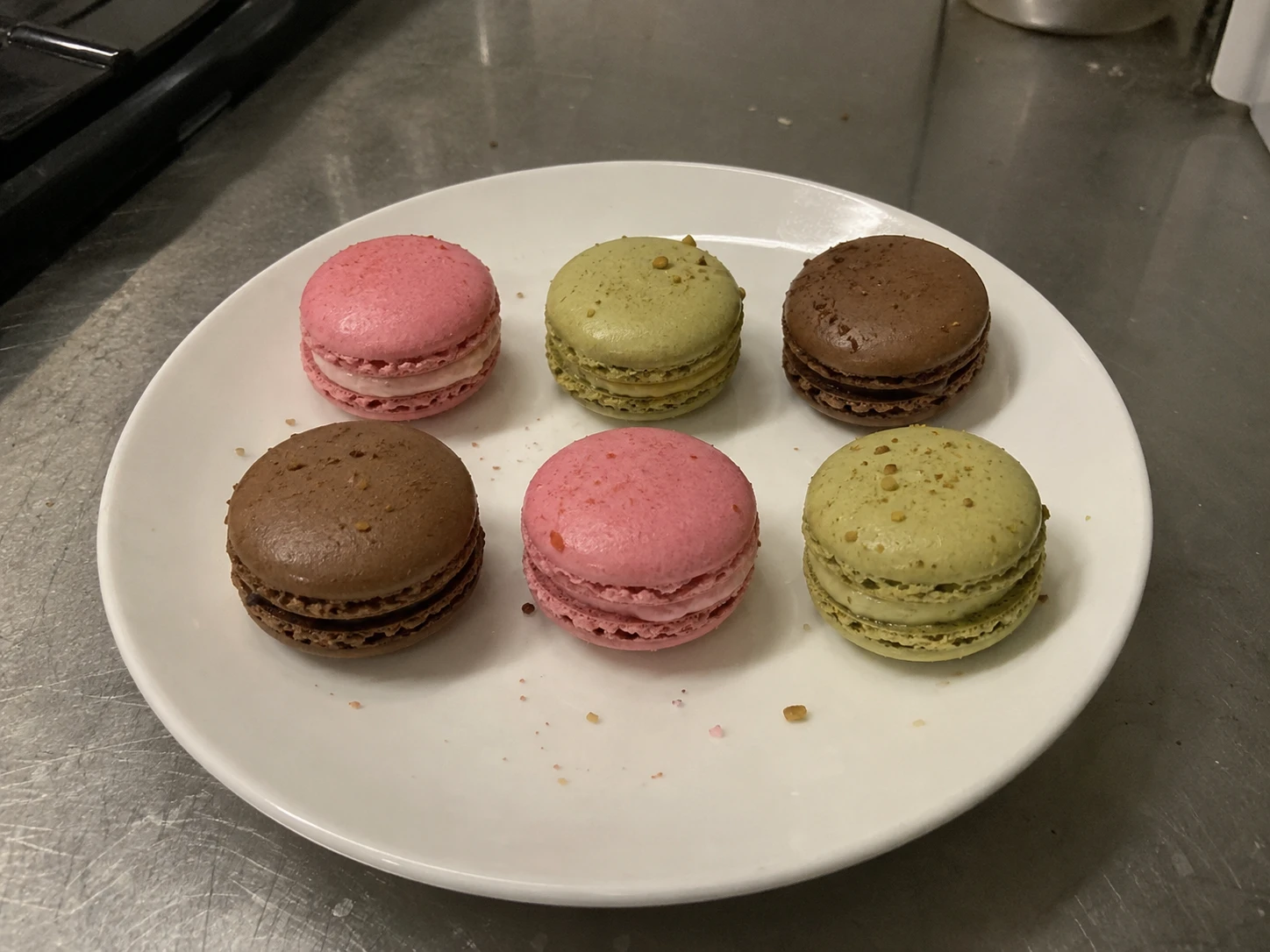 The same six macarons on a plate in a dim, unstyled kitchen photo